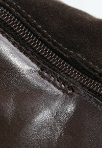 Gros plan d'une surface en cuir et en daim brun foncé avec des coutures visibles et une fermeture éclair métallique.