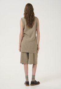 Beige sleeveless top with a longer back, paired with loose matching shorts. Textured fabric, flat seams, and ankle-high socks with shoes.