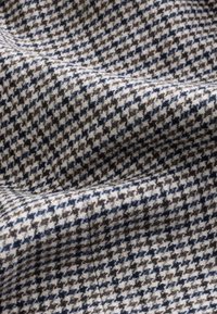 Close-up of textured fabric with gray, black, and navy blue houndstooth pattern showing soft folds and woven fibers.