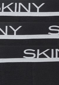 Intimo nero con una larga vita elastica bianca che presenta il nome del marchio "SKINY" in lettere maiuscole. Tessuto morbido e liscio.