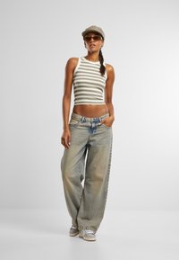 Striped crop top in olive and cream, paired with light-wash wide-leg jeans. Gray cap and sunglasses complete the outfit. Casual style.