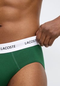 Πράσινο βαμβακερό εσώρουχο Lacoste με λευκή ελαστική μέση που φέρει μαύρο λογότυπο. Κοντινή λήψη που αν αδεικνύει την υφή του υφάσματος.