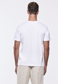 Bílá bavlněná tričko s kulatým výstřihem a krátkými rukávy, zobrazeno z pohledu na zadní stranu. Tkanina vypadá hladce a lehce.