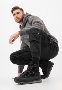 Černé turistické boty se šněrováním, šedá mikina a černé cargo kalhoty. Texturované materiály s mírně polstrovaným vzhledem a slim fit střihem.