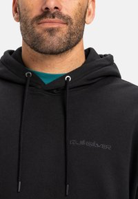 Black hoodie made of cotton blend, featuring a simple design, metal eyelets, and a subtle embroidered logo on the front.