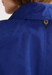 Chemise de travail à texture lisse, dotée d'un patch logo triangulaire et d'accents contrastants.