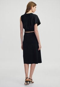 Zwart tweedelig outfit met een cropped top met asymmetrische stof en een midi rok. De textuur is soepel met een getailleerd silhouet.