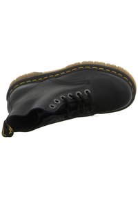 Botte noire en cuir à lacets avec surpiqûres jaunes et une semelle en caoutchouc translucide dotée d'une languette jaune au talon.