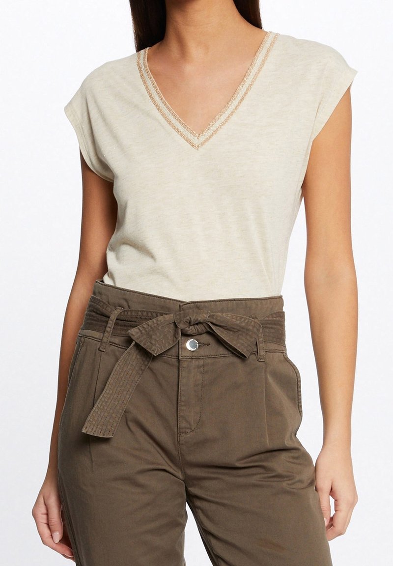 Beige V-neck top with cap sleeves and intricate lace trim, paired with high-waisted olive green trousers featuring a bow tie belt.