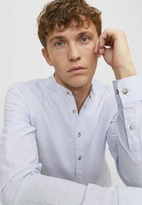 Camicia a strisce blu chiaro con colletto alla cinese, dettagli con bottoni e maniche lunghe arrotolate ai polsi. Tessuto dalla texture liscia.