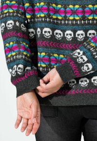 Grauer Pullover mit bunten Mustern, die Schädel, Blumen und geometrische Designs zeigen. Gerippte Bündchen in Schwarz und Pink. Weicher Stoff.