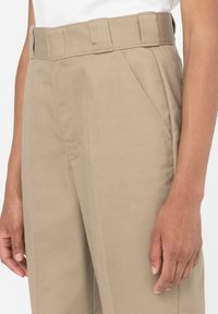 Krémové kalhoty s vysokým pasem, hladkým předním dílem a bočními kapsami. Vyrobené z hladkého materiálu, s poutky na opasek a rovnými nohavicemi.