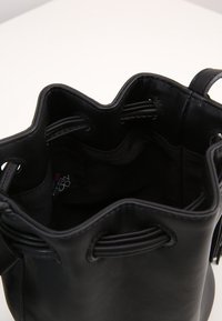 Borsa a secchiello nera in pelle con superficie strutturata, chiusura a coulisse e fodera liscia. L'interno presenta un etichetta colorata del marchio.