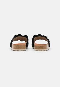 Zwarte suede sandalen met een scalloped bandontwerp, kurken voetbed en rubberen buitenzool. Open achterkant voor eenvoudig aan- en uittrekken.
