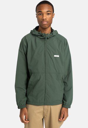 Grüne leichte Jacke mit einem Reißverschluss vorne, verstellbarem Kapuzen und elastischen Bündchen. Hat ein kleines Logo und Seitentaschen.