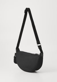 Bolso cruzado de nylon negro con un diseño curvado, correa ajustable, herrajes de plata y cierre con cremallera. Presenta el nombre de la marca en relieve.