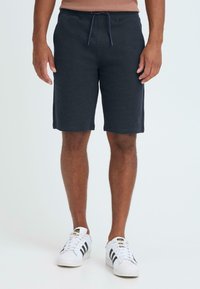 Shorts bleu marine en tissu texturé, dot és d'une taille élastique avec un cordon de serrage et des poches latérales. Portés avec des baskets blanches.