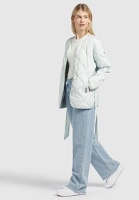 Licht mintgroene geborduurde jas met een ontspannen pasvorm, knoopsluiting en zijbanden, gecombineerd met lichtblauwe wijde jeans en witte sneakers.