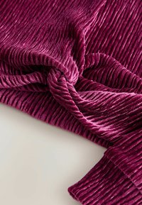 Zerknitterter Samtstoff, tief magentafarben, mit einer gerippten Textur, weichen Falten und einer glatten Oberfläche, ideal zum Drapieren oder für Kleidung.