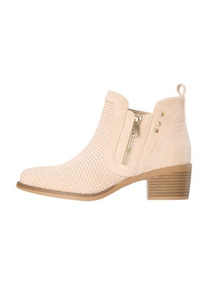 Bottine en daim beige avec design perforé, fermeture éclair latérale, trois clous dorés au talon, talon bloc en bois superposé et languette à l'arrière.