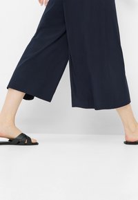 Navy wide-leg trousers made of lightweight fabric, featuring a loose fit and cropped length, paired with black strappy sandals.