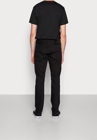 Camiseta de algodón negra y pantalones vaqueros negros de mezclilla llevados juntos, vistos desde atrás. Los pantalones tienen dos bolsillos traseros y un ajuste ceñido.