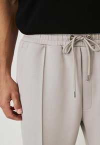 Light gray joggers with an elastic waistband, drawstring fastener, and side pockets. Smooth texture with subtle pleats near the waist.