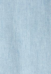 Light blue denim fabric with visible diagonal weave texture and subtle variations in thread color and shading.