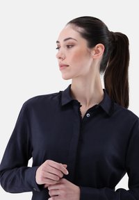 Navy blue shirt with a collar featuring frayed edges, button placket, and a smooth texture. The model is facing sideways, hair in a ponytail.