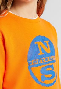 Sudadera naranja con un gráfico azul que presenta las letras "N" y "S" y el texto "NORTH SAIL" en un diseño circular. Textura suave.