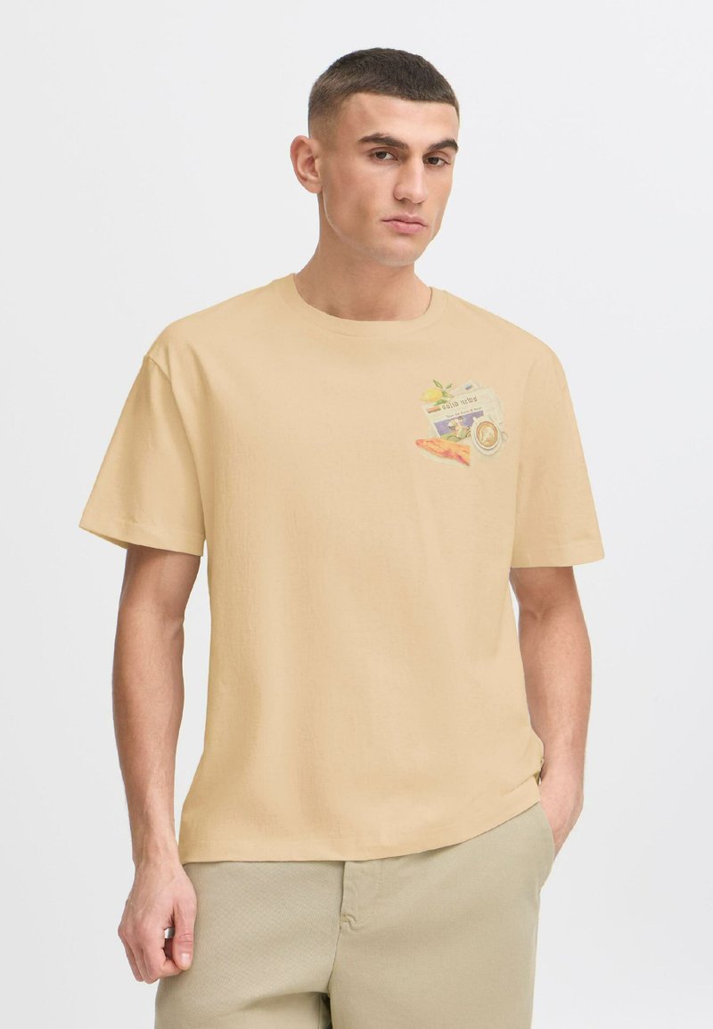Short-sleeve, beige cotton t-shirt featuring a small graphic of fruits and a newspaper-style design printed on the left chest area.
