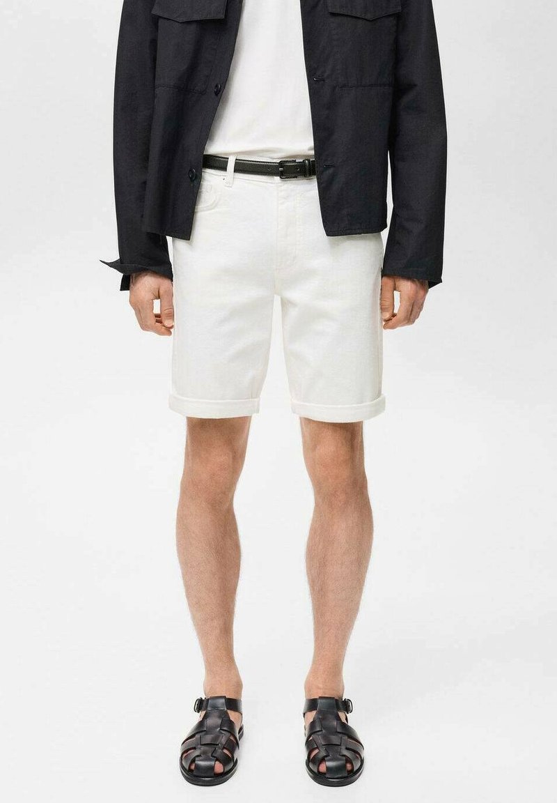 Shorts en denim blanc avec des ourlets roulés, associés à une veste noire à boutons et des sandales tissées noires. Design minimaliste, texture lisse.
