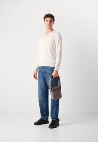 Maglione a V in crema, jeans blu sbiaditi, sneakers nere. Tiene una piccola borsa marrone con logo "BOSS" e tracolla regolabile.