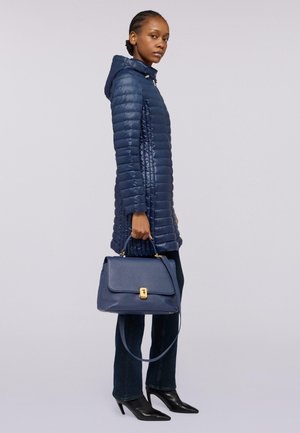 Manteau d'hiver bleu marine matelassé avec une capuche, assorti d'un sac à main structuré bleu marine avec un fermoir et une poignée dorés. Escarpins noirs à bout pointu.