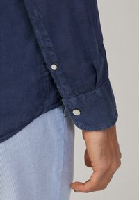 Camicia a maniche lunghe blu navy con polsini a bottoni, realizzata in un tessuto testurizzato, abbinata a pantaloni a righe orizzontali blu chiaro.