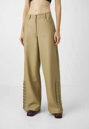 Bredde bukser i beige faux skinn med en glatt tekstur. Har frontlommer og snøring ved anklene med metalløye.