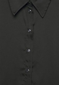 Černá košile na knoflíky s špičatým límcem, vyrobená z hladké strukturované látky a s černými knoflíky na přední legu.