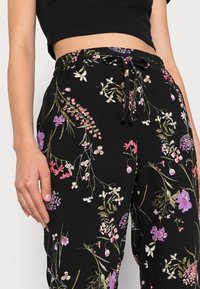 Svarta blommiga byxor med dragsko i midjan, med färgglada blommönster i nyanser av rosa, lila och grönt på en strukturerad tyg.