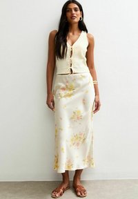 Un crop top a coste color crema con un nodo frontale, abbinato a una gonna in satin lunghezza pavimento con un motivo floreale in rosa chiaro e giallo.