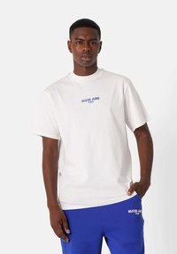 Hvid bomulds t-shirt med korte ærmer, som har blå tekst "SIXTH JUNE" og "PARIS" på brystet. Glat tekstur, afslappet pasform.
