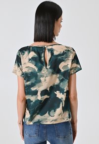 Top a maniche corte in verde scuro e beige con un motivo a nuvola, caratterizzato da un dettaglio con apertura a chiave sul retro, fissato con un bottone.