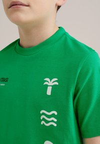 Zielony bawełniany T-shirt z okrągłym dekoltem, białymi nadrukami przedstawiającymi palmę, fale oraz tekst na piersi, z krótkimi rękawami.