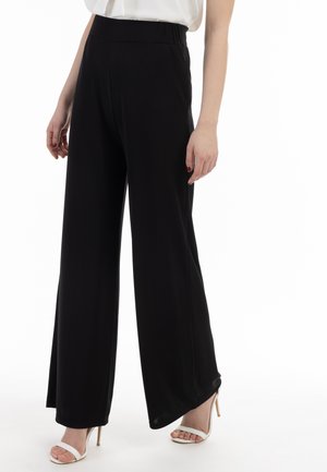Pantaloni neri a gamba larga realizzati in un tessuto morbido. Presentano una vita elastica e un fit rilassato, abbinati a sandali bianchi con tacco alto.