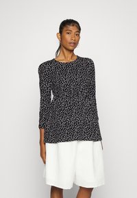 Blusa preta com bolinhas brancas, decote redondo, mangas longas e design peplum, combinada com calções largos brancos texturizados.