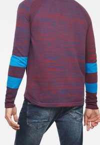 Chemise à manches longues bordeaux et bleue avec des rayures texturées ; présente des rayures bleues contrastantes sur les manches et un ourlet arrondi.