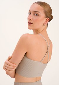 Rippierter beige Sport-BH mit schmaler Passform, dünnen verstellbaren Trägern und gekreuztem Rücken. Glatte Stofftextur ohne sichtbare Beschläge.