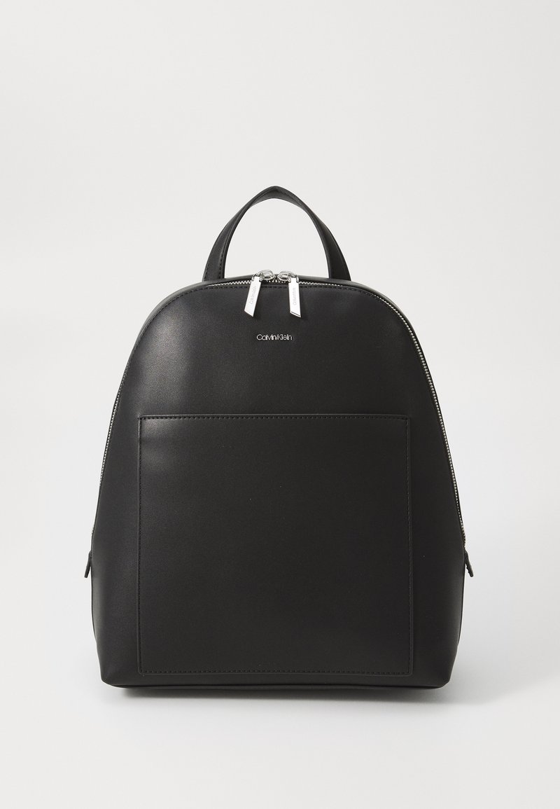Black leather backpack with a rounded shape, front pocket, dual silver zippers, and a top handle for carrying. Minimalist design.