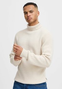Beige garbónyakú pulóver bordázott textúrával, hosszú ujjal és laza szabással. Tiszta varrási részlet és oldalsó hasíték az alján.
