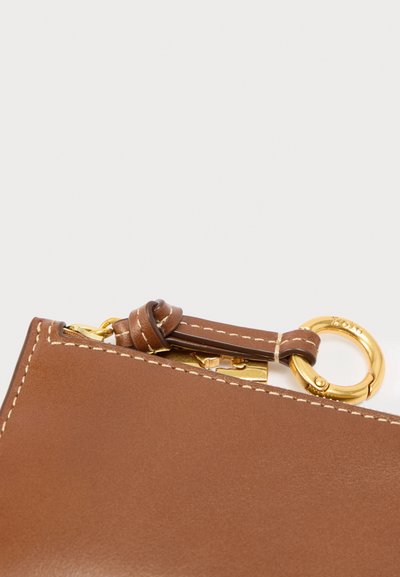 Canto de uma mala em pele castanha com um anel de ferragem dourado e tira, com costura clara contrastante ao longo da borda.