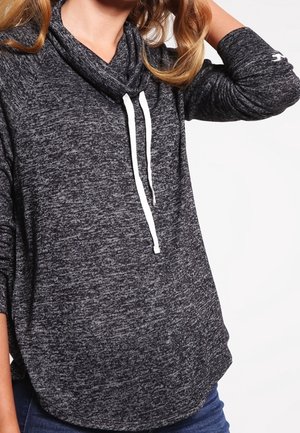 Sweat-shirt gris marbré avec un col cheminée, doté de cordons blancs et de manches longues, porté avec un jean bleu sur un fond uni.